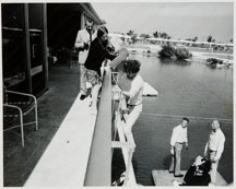Woman comes up the ladder from the floating dock where the dolphions perform.  The villa colony is in the distance.